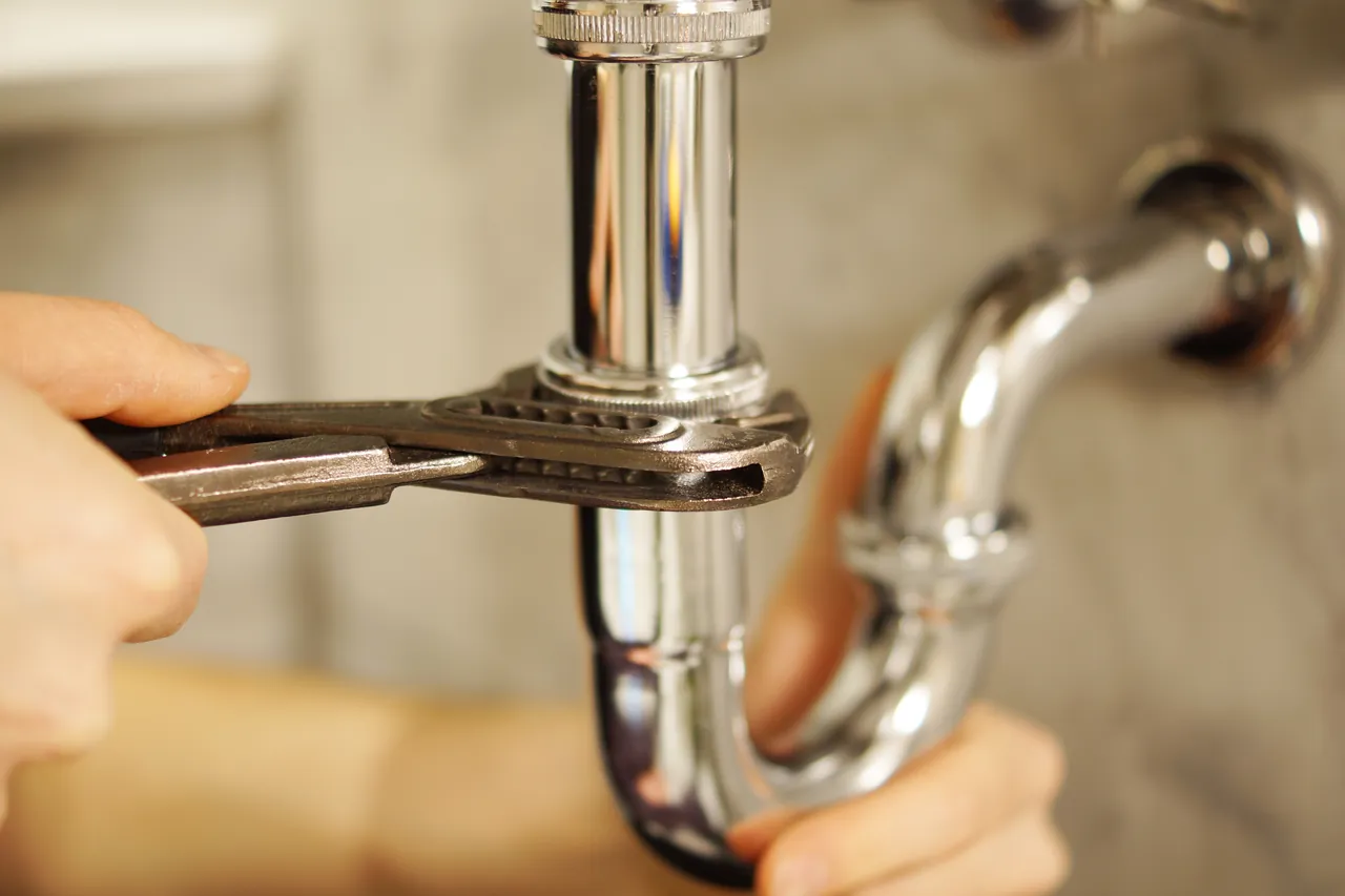 Hände ziehen mit der Wasserpumpenzange den Siphon unter einem Waschbecken nach